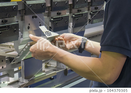 Close up the bending machine operator hold the sheet metal parts. Close up the bending machine operator hold the sheet metal parts. 104370305