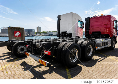 Back view many new heavy commercial cargo transport vehicles stand at port for export import shipping in Germany. Modern semi-trailer business industry truck tractor chassis sale sea logistics 104370371
