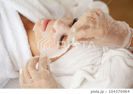 Cosmetologist applying sheet mask on woman in spa beauty salon 104370964