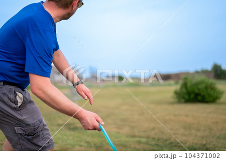Selective focus on a Caucasian adult preparing to sidearm throw a disc golf towards the pin.  104371002