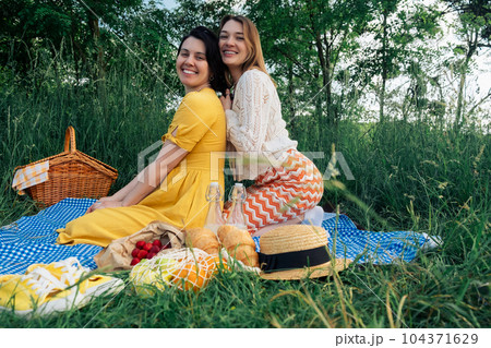 Two girls on a date sit on a blue blanket for a picnic in nature Two girls on a date sit on a blue blanket for a picnic in nature 104371629