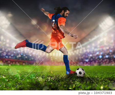 Soccer scene at night match with player in a orange uniform kicking the ball with power Soccer scene at night match with player in a orange uniform kicking the ball with power 104371983