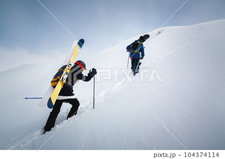 Backcountry climbers walking with skis in the mountains. Ski tourism in alpine landscape with snowy mountains. Adventure winter sport 104374114