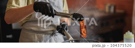 Close-up view of chef in uniform stir frying bacon in pan for cooking dish in restaurant kitchen Close-up view of chef in uniform stir frying bacon in pan for cooking dish in restaurant kitchen 104375520