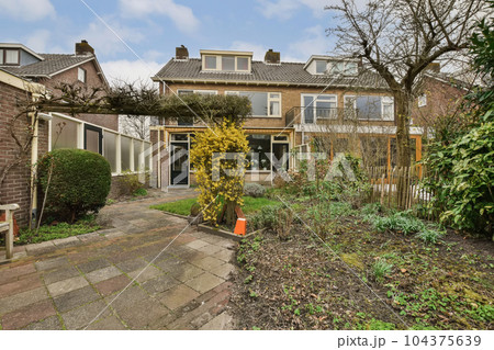 a house in the netherlands, with trees and plants growing on either side of the house there is a small garden a house in the netherlands, with trees and plants growing on either side of the house there is a small garden 104375639