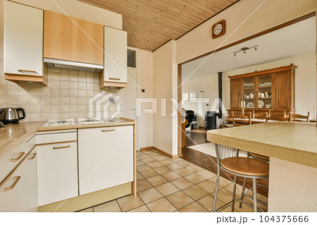 a kitchen and dining area in a small apartment with wood paneled ceilings, tile flooring and white cabinets 104375666