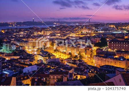 Night view of Lisbon famous view from Miradouro da Senhora do Monte tourist viewpoint of Alfama and Mauraria old city districts, 25th of April Bridge in the evening twilight. Lisbon, Portugal 104375740
