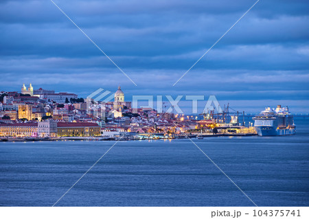 View of Lisbon over Tagus river with passing ferry boat from Almada with moored cruise liner in evening twilight. Lisbon, Portugal 104375741