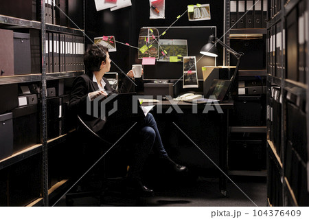 Private detective holding criminal investigations case files, analyzing crime evidence trying to catch mysterious suspect. Fbi investigator checking victim report late at night in arhive room 104376409