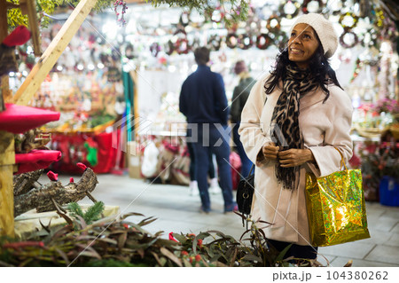 Hispanic woman choosing fir tree decorations at street Christmas fair 104380262