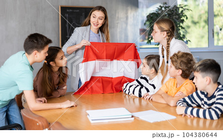 Teacher showing Austria flag to group of preteen schoolchildren 104380644