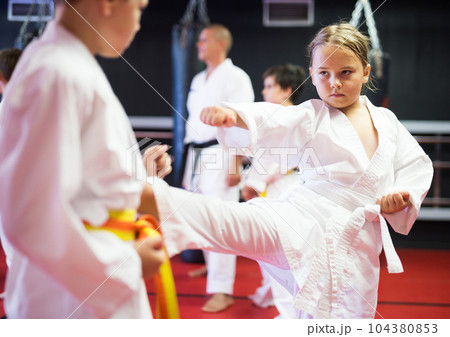 Children practicing in pair karate movements with male trainer supervision 104380853