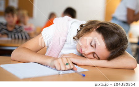 Girl is tired and sleeping at the desk in classroom 104380854