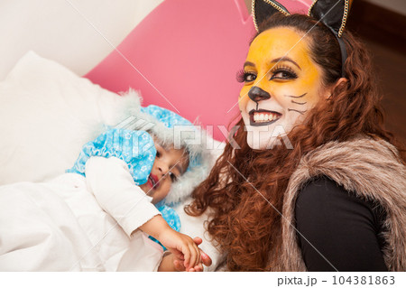 Mother playing wolf character and little girl playing grandma. Real family having fun while using costumes of the Little red riding hood tale in Halloween. Mother playing wolf character and little girl playing grandma. Real family having fun while using costumes of the Little red riding hood tale in Halloween. 104381863