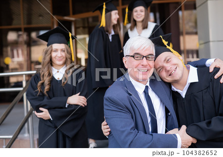 A gray-haired male teacher congratulates students on their graduation from the university.  104382652