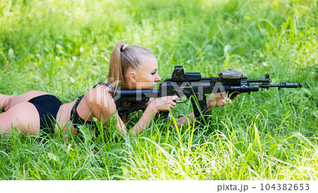 Caucasian woman in bikini lies with machine gun on green grass. Caucasian woman in bikini lies with machine gun on green grass. 104382653