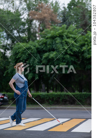 Blind pregnant woman crosses the road at a crosswalk with a cane.  104382807