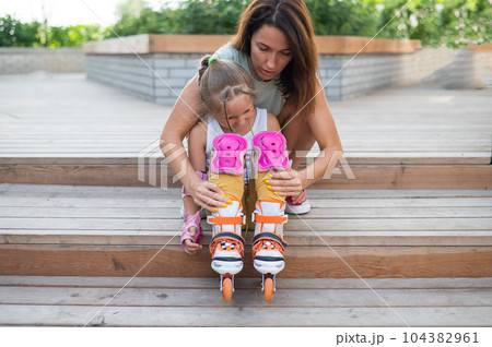 Little girl in roller skates and her mom sit on a wooden ladder and hug outdoors.  104382961