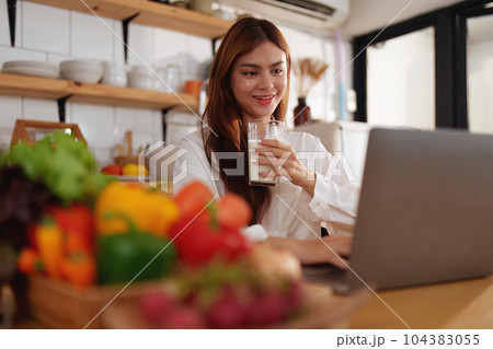 Portrait of a young cheerful asian woman drinking milk in kitchen room with healthy raw food. Vegetarianism, wellbeing and healthy lifestyle concept Portrait of a young cheerful asian woman drinking milk in kitchen room with healthy raw food. Vegetarianism, wellbeing and healthy lifestyle concept 104383055
