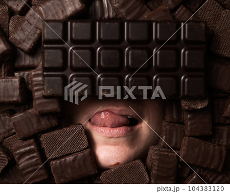 The face of a caucasian woman surrounded by chocolates. girl showing tongue.  104383120