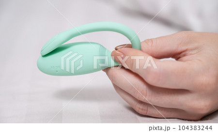 Woman holding mint vibrator while lying on white sheet. Woman holding mint vibrator while lying on white sheet. 104383244