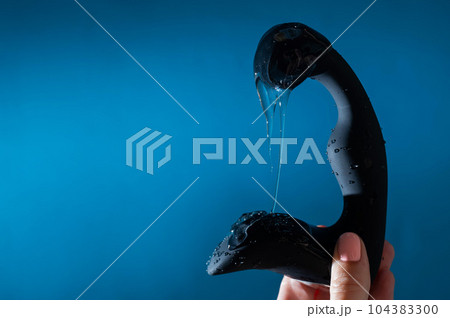 A woman pours lubricant on a black prostate stimulator on a blue background. Men's health prevention concept. A woman pours lubricant on a black prostate stimulator on a blue background. Men's health prevention concept. 104383300