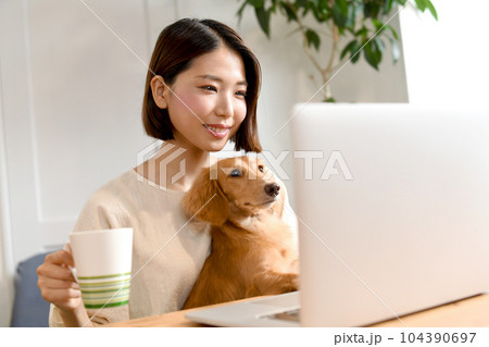 犬を抱きながらパソコン操作をする若い女性 104390697
