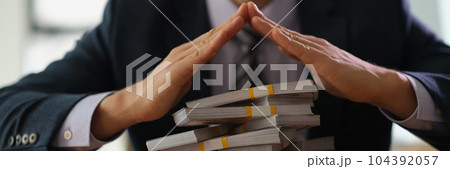 Banker making roof with hands over bundles of dollar bills closeup Banker making roof with hands over bundles of dollar bills closeup 104392057