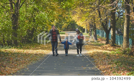 A happy young family walks along a city park road in the fall. A happy young family walks along a city park road in the fall. 104392499