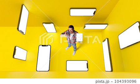 Conceptual design. Man with 3d mobile phone screens over yellowbackground. Online shopping and services. E-commerce Conceptual design. Man with 3d mobile phone screens over yellowbackground. Online shopping and services. E-commerce 104393096