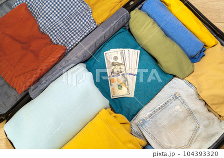 Open suitcase with women's clothing for holidays and a stack of dollars Open suitcase with women's clothing for holidays and a stack of dollars 104393320
