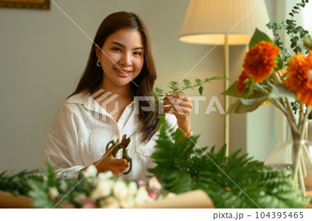 Attractive young housewife creating beautiful bouquet with different flowers in cozy home Attractive young housewife creating beautiful bouquet with different flowers in cozy home 104395465