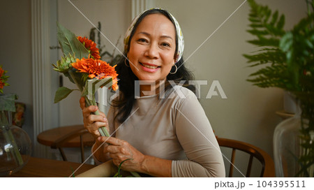 Positive middle age woman holding beautiful bouquet and smiling to camera. Retirement, floristry and small business concept Positive middle age woman holding beautiful bouquet and smiling to camera. Retirement, floristry and small business concept 104395511
