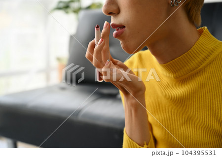 Young gay man doing daily makeup in living room with rainbow flag on background. LGBTQ, lifestyle and makeup concept 104395531