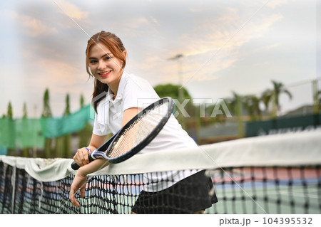 Beautiful sportswoman holding racket and standing near net on the tennis court. Fitness, sport and competition concept Beautiful sportswoman holding racket and standing near net on the tennis court. Fitness, sport and competition concept 104395532