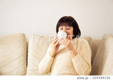 Good looking relaxed senior woman in good mood drinking a cup of coffee or hot tea at home. 104399156