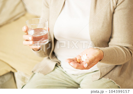 Middle aged unrecognized woman sitting at home, holding glas of fresh water and taking medicine. Middle aged unrecognized woman sitting at home, holding glas of fresh water and taking medicine. 104399157