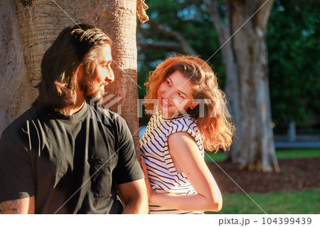 木の陰から覗く彼女とにこやかに見る彼氏 104399439