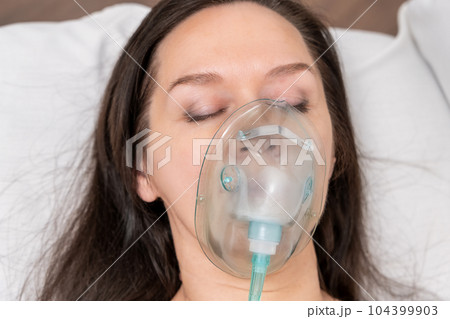 An adult woman lies on a hospital bed in an oxygen mask and undergoes treatment. 104399903