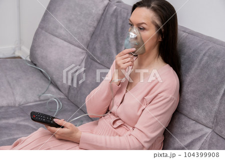 The woman inhales the respiratory tract and lungs when applying drugs. A woman breathes through a face mask using a nebulizer. The woman inhales the respiratory tract and lungs when applying drugs. A woman breathes through a face mask using a nebulizer. 104399908