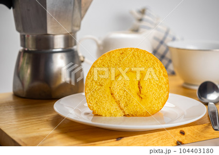 Side view coffee time with delicious homemade cake roll filled with pineapple jam in white ceramic plate. 104403180