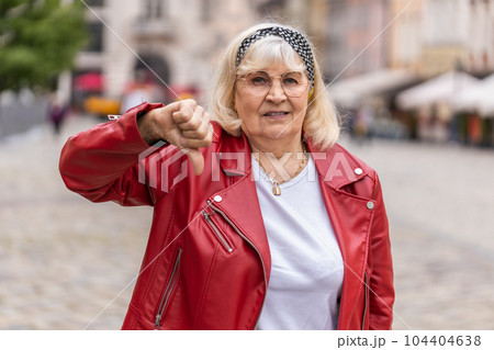 Upset senior woman showing thumbs down sign, disapproval, dissatisfied bad work, mistake in city 104404638