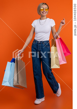 Delighted woman in white t shirt and jeans enjoying shopping holding bags 104408500