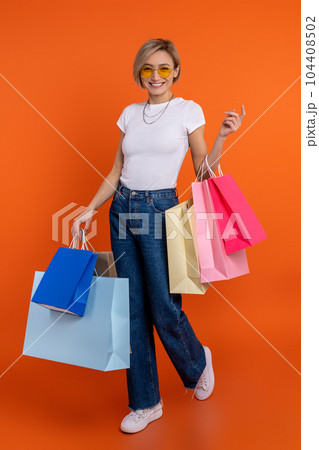 Overjoyed woman in white t shirt and jeans standing with shoppingbags 104408502