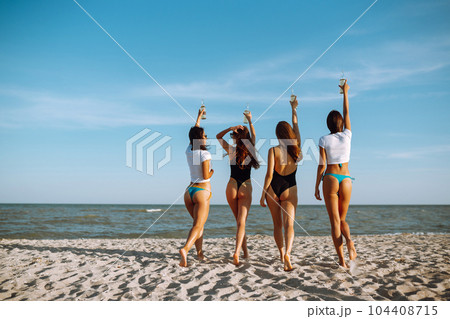Four young girlfriends with beers in their hands raised together enjoying a holiday on the sea shore. Four young girlfriends with beers in their hands raised together enjoying a holiday on the sea shore. 104408715