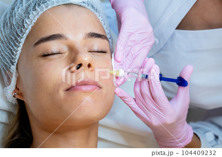 PRP ttherapy in beauty clinic, cosmetologist doing injections to woman's face to cure problem skin. 104409232