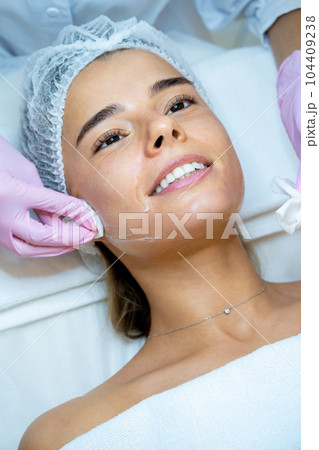 Beautician's hands cleaning female face with cotton pads at aesthetic clinic. 104409238
