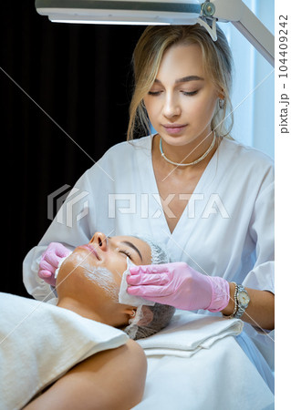 Blonde beautician doctor cleaning woman face with cotton pads, skin care procedures, rejuvenation. 104409242