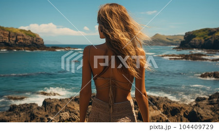 Young woman seen from behind standing looking at the sea during the sunset. 104409729
