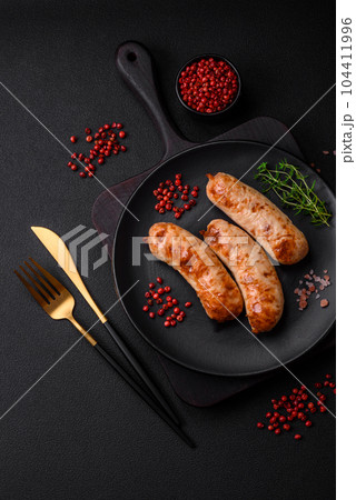 Delicious juicy grilled sausages with salt, spices and herbs on a ceramic plate Delicious juicy grilled sausages with salt, spices and herbs on a ceramic plate 104411996